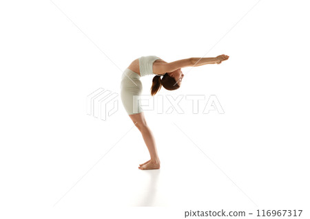 Fit woman wearing fit wear stands in yoga pose, stretching against white studio background. 116967317