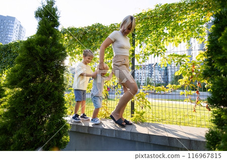 Mother Enjoys Fun Outdoor Playtime With Her Two Sons at the Local Playground in the Afternoon 116967815