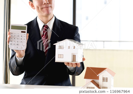 一位身穿西裝的亞洲男性商人擔心房屋模型和計算器。 116967964