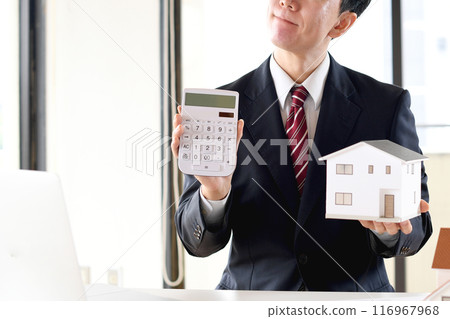 一位身穿西裝的亞洲男性商人擔心房屋模型和計算器。 116967968