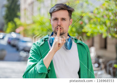 Man presses index finger to lips makes silence hush gesture sign do not tells gossip secret outdoors 116968553