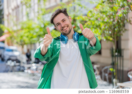 Happy man tourist showing thumbs up like positive something good positive feedback on city street Happy man tourist showing thumbs up like positive something good positive feedback on city street 116968559