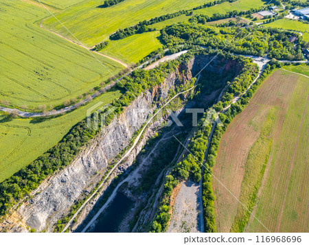An aerial view captures the scenic beauty of the deserted Velka Amerika limestone quarry in Czechia, surrounded by lush greenery and farmland. 116968696