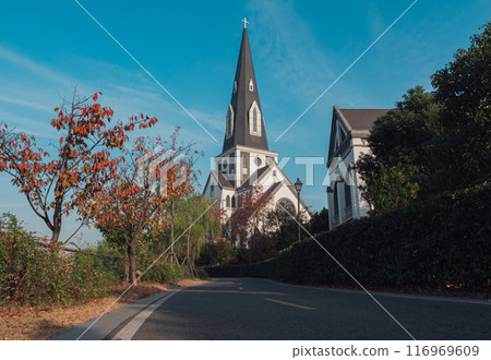 Charming white church with steeple surrounded by colorful autumn foliage on a clear day 116969609