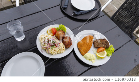 Seafood restaurant on the seashore. White plate with fish patties, fish fillets and potato salad. 116970318