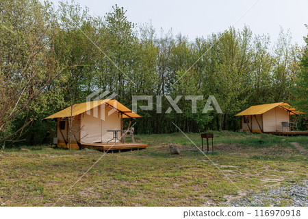 Cozy open glamping tents with light inside in summer camp. Camping tent for holiday and vacation Cozy open glamping tents with light inside in summer camp. Camping tent for holiday and vacation 116970918
