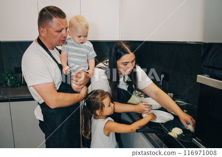 A happy family is enjoying the fun of cooking together in a modern, collaborative kitchen. Happy family enjoys moments of cooking at home. 116971008