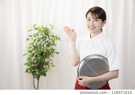 A smiling female cafe staff member holding a silver tray 116971818