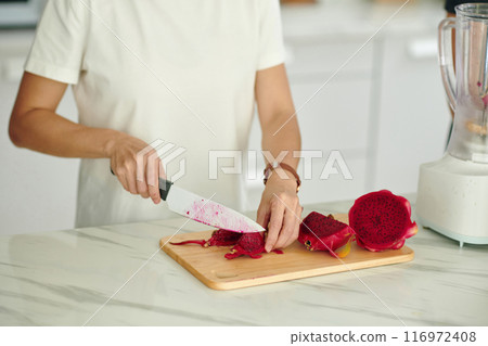 Slicing Dragon Fruit with Sharp Knife on Wooden Cutting Board 116972408