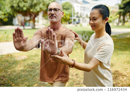 Practicing Tai Chi With Instructor in Public Park Setting 116972434
