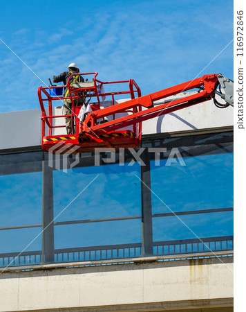 Elevated pedestrian overground tunnel facade painting using a telescopic boom lift with a basket Elevated pedestrian overground tunnel facade painting using a telescopic boom lift with a basket 116972846