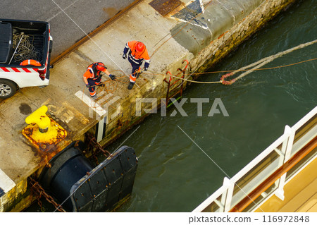 The process of mooring a large ship at the harbor pier, pulling the rope ashore 116972848