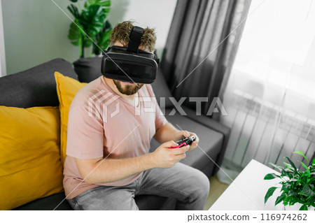 Man playing video games in living room sitting on sofa. Man playing video games in living room sitting on sofa. 116974262