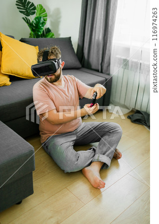 Man playing video games in living room sitting on sofa. Man playing video games in living room sitting on sofa. 116974263