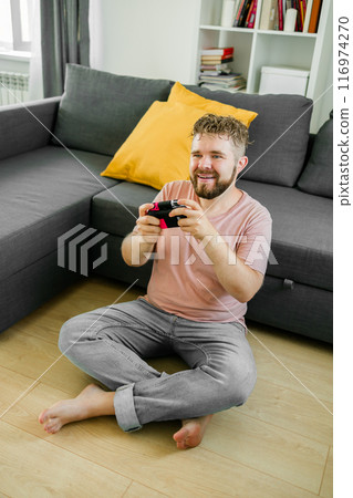 Man playing video games in living room sitting on sofa. Man playing video games in living room sitting on sofa. 116974270