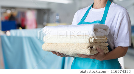 Cleaning woman in blue apron holding towels. 116974333