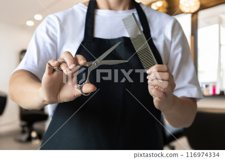 Hairdresser in black apron holding scissors and comb . 116974334