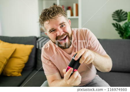 Man playing video games in living room sitting on sofa. 116974980