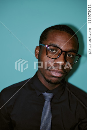 Vertical flash shot portrait of young African American male employee wearing eyeglasses looking at camera, blue background 116975011