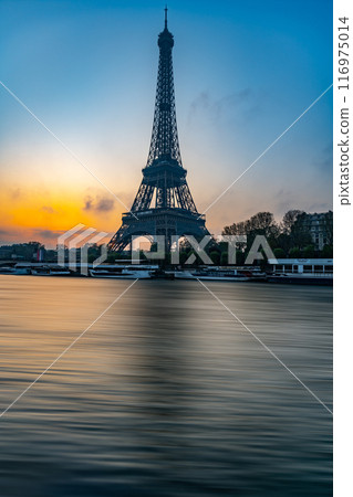 The Eiffel Tower stands majestically against a colorful morning sky as the sun rises, casting reflections on the calm waters of Seine River nearby. The Eiffel Tower stands majestically against a colorful morning sky as the sun rises, casting reflections on the calm waters of Seine River nearby. 116975014