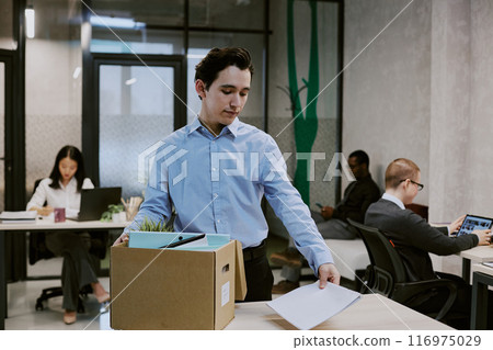 Medium shot of new recruit standing at office desk preparing his workspace on first workday, copy space 116975029