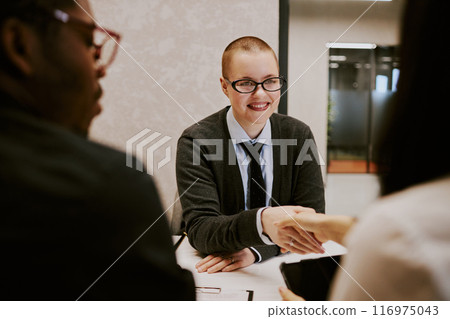 Over shoulder shot of cheerful young woman with buzz cut doing handshake with business partner during meeting Over shoulder shot of cheerful young woman with buzz cut doing handshake with business partner during meeting 116975043