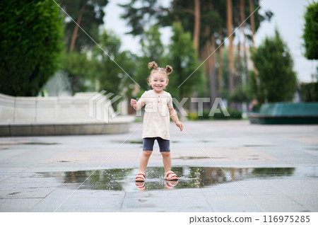Toddler girl jumping through puddles in summer 116975285