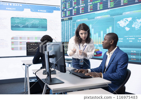 Diverse teammates examining statistics and infographics on computer in control room, joining forces to gather insight for business development. Analysts discussing legal changes. Diverse teammates examining statistics and infographics on computer in control room, joining forces to gather insight for business development. Analysts discussing legal changes. 116975483