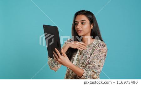 Upbeat woman having friendly conversations during teleconference meeting using tablet, studio background. Person having fun catching up with mates during online videocall on digital device, camera A Upbeat woman having friendly conversations during teleconference meeting using tablet, studio background. Person having fun catching up with mates during online videocall on digital device, camera A 116975490