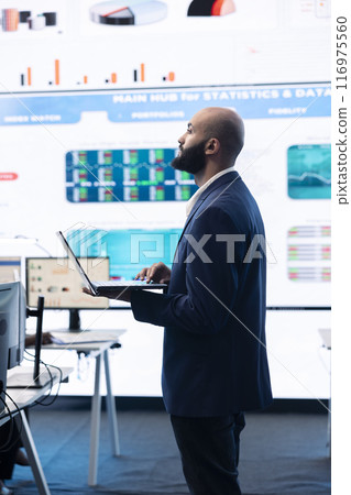 Administrative assistant examining important big data visualizations on a huge display, creating an analysis to review key performance indicators and business efficiency in office. 116975560