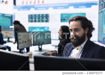 CEO reviewing business activity numbers on annual reports in control room, examining progress status and infographics. Finance advisor looks into big data analytics online at pc. CEO reviewing business activity numbers on annual reports in control room, examining progress status and infographics. Finance advisor looks into big data analytics online at pc. 116975577