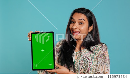 Portrait of indian woman doing influencer marketing using green screen tablet, isolated over studio background. Smiling person holding empty copy space mockup device, camera B Portrait of indian woman doing influencer marketing using green screen tablet, isolated over studio background. Smiling person holding empty copy space mockup device, camera B 116975584