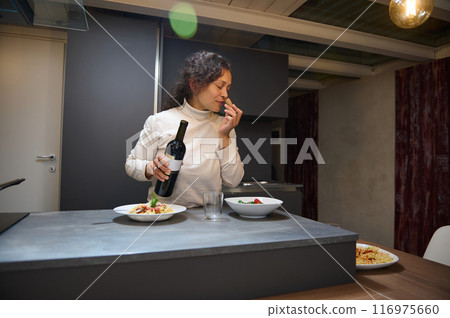 Woman enjoying pasta meal with red wine in modern kitchen 116975660