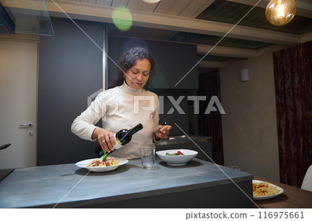 Woman pouring wine in a modern kitchen while preparing dinner 116975661