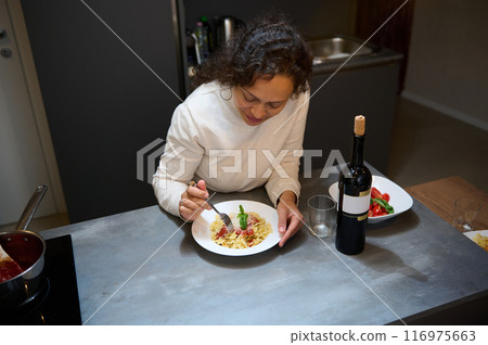 Woman enjoying homemade pasta dinner with bottle of wine in modern kitchen setting 116975663