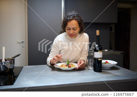 Woman enjoying a meal with wine in a modern kitchen setting 116975667