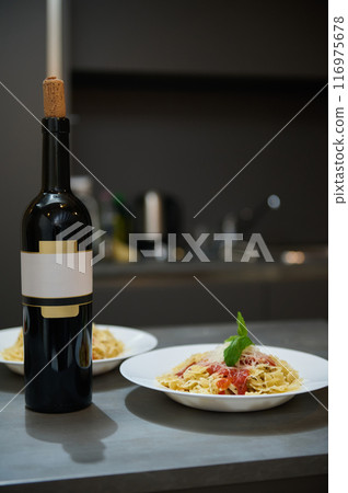 Elegant dinner setup with bottle of wine and pasta plates in a modern kitchen Elegant dinner setup with bottle of wine and pasta plates in a modern kitchen 116975678