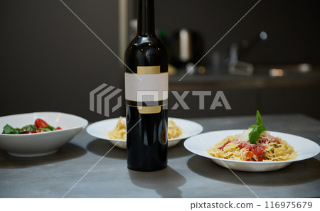 Elegant dinner setting with wine bottle and pasta dishes in a modern kitchen Elegant dinner setting with wine bottle and pasta dishes in a modern kitchen 116975679