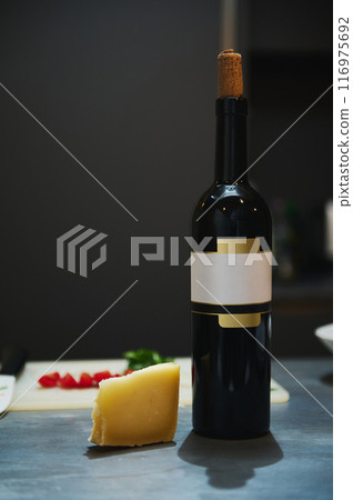 Bottle of red wine with cork and cheese wedge on kitchen countertop 116975692