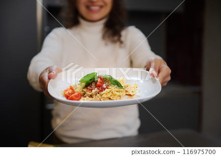 Smiling woman presenting a delicious plate of pasta with fresh tomatoes and basil 116975700
