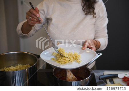 Woman serving pasta on a plate in a home kitchen 116975713