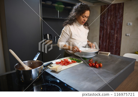 Woman preparing a meal in a modern kitchen with fresh ingredients on a cutting board 116975721