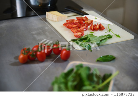 Fresh tomatoes and leafy greens on a cutting board in a modern kitchen setting 116975722