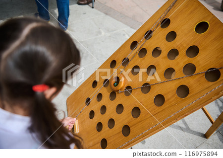 Child playing a wooden marble maze game at an outdoor event Child playing a wooden marble maze game at an outdoor event 116975894