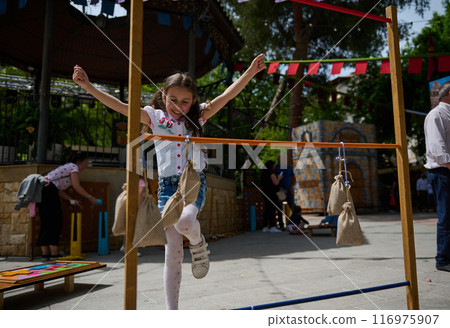 Young girl enjoying outdoor festival game with burlap sack obstacles on a sunny day Young girl enjoying outdoor festival game with burlap sack obstacles on a sunny day 116975907