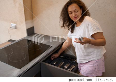 Woman in modern kitchen organizing silverware drawer, casual home scene Woman in modern kitchen organizing silverware drawer, casual home scene 116976079