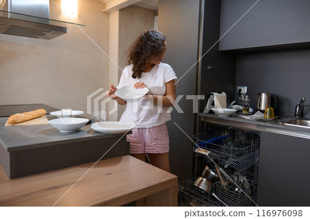 Woman unloading dishwasher and setting table in modern kitchen 116976098