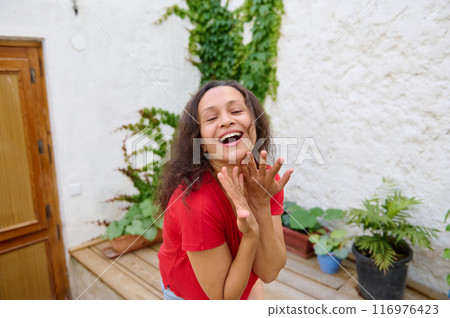 Joyful woman in red shirt laughing and enjoying outdoor garden space Joyful woman in red shirt laughing and enjoying outdoor garden space 116976423
