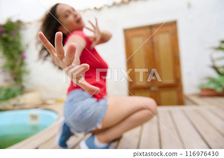 Young woman playfully reaching towards the camera in a vibrant outdoor setting Young woman playfully reaching towards the camera in a vibrant outdoor setting 116976430