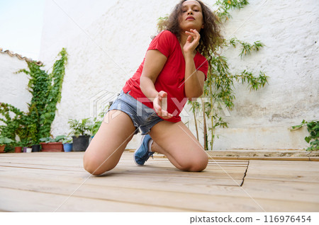 Young woman dancing passionately on outdoor wooden deck surrounded by plants 116976454